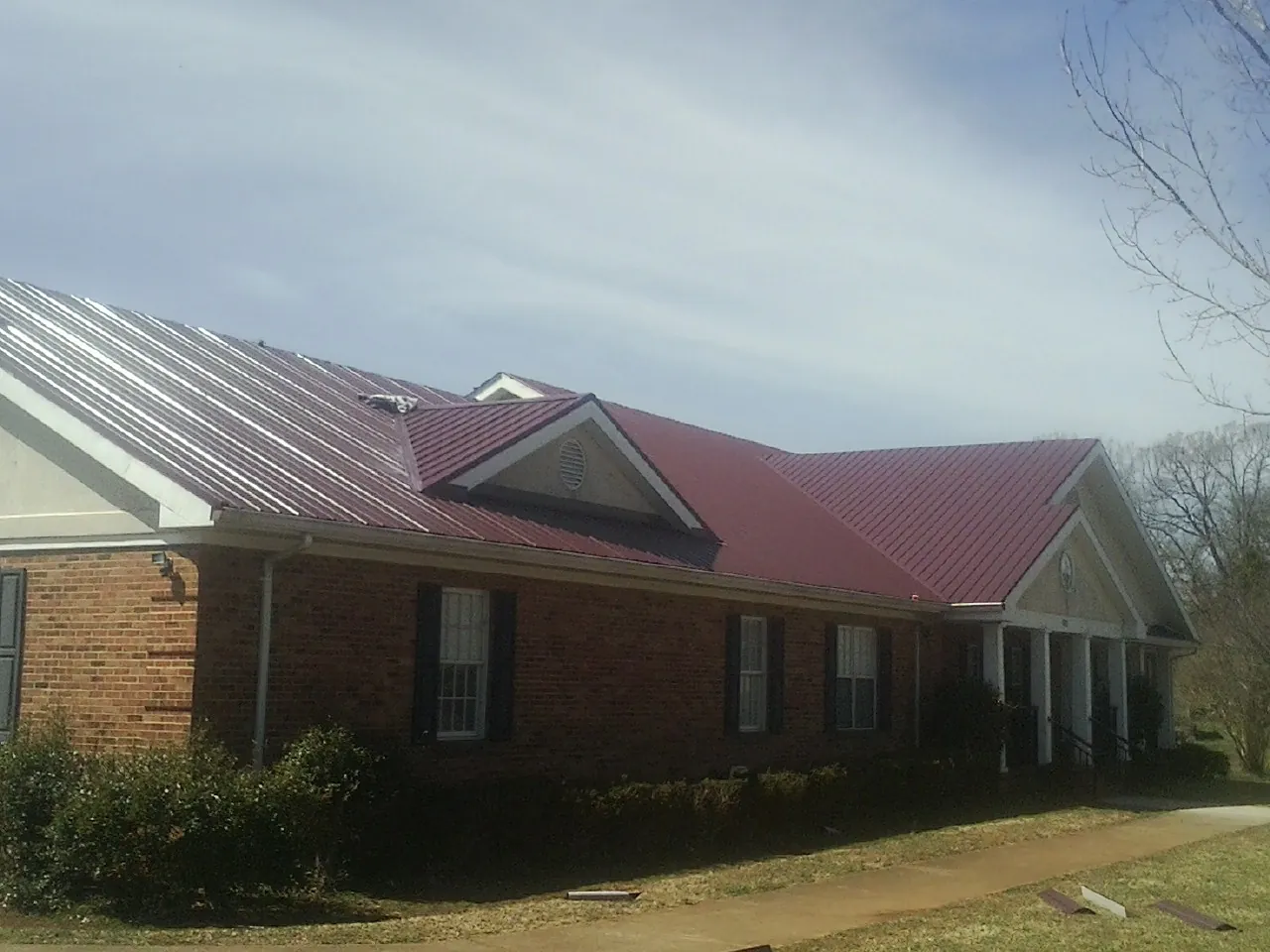 Red metal roof with gabled entries on a long brick building, from a Hail Damage Roof Repair job in Wauchula