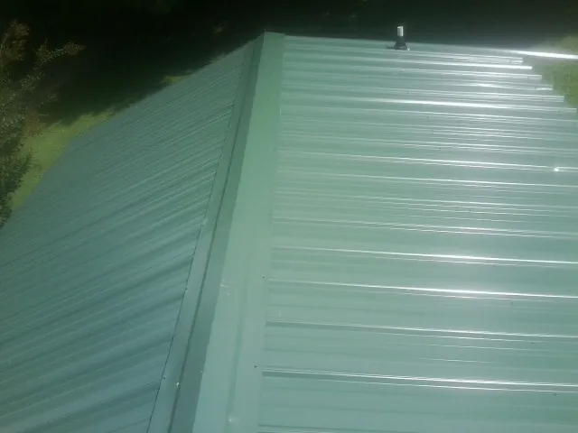 New green metal panels meeting at the ridge of a roof — Flat Roof Repair work by our crew in Wauchula